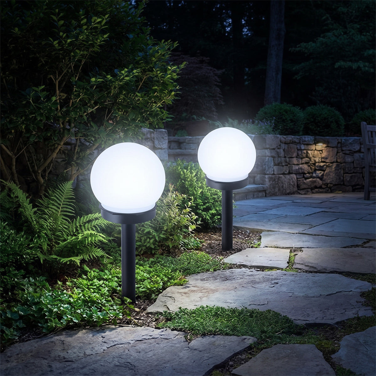 Two solar globe stake lights with cool white light beside a stone path at night