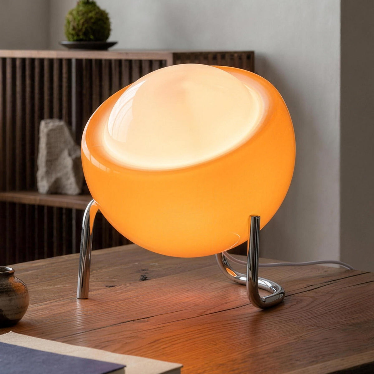 Solveig table lamp with an orange glass globe, lit on an oak desk