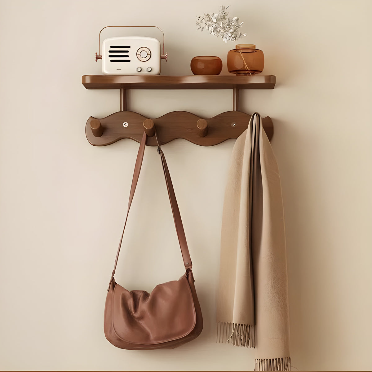 Sonja wall rack in brown with four pegs holding a bag and a scarf, a radio and vases on the shelf