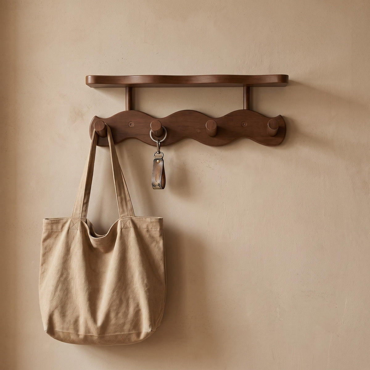 Bamboo pegs of the Sonja wall rack holding a bag and a key ring in a hallway