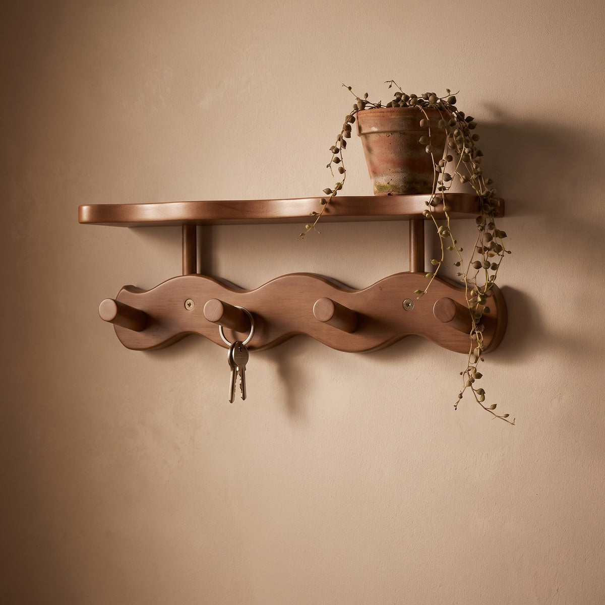 Sonja wall rack in brown with a trailing plant on its shelf and keys on a peg