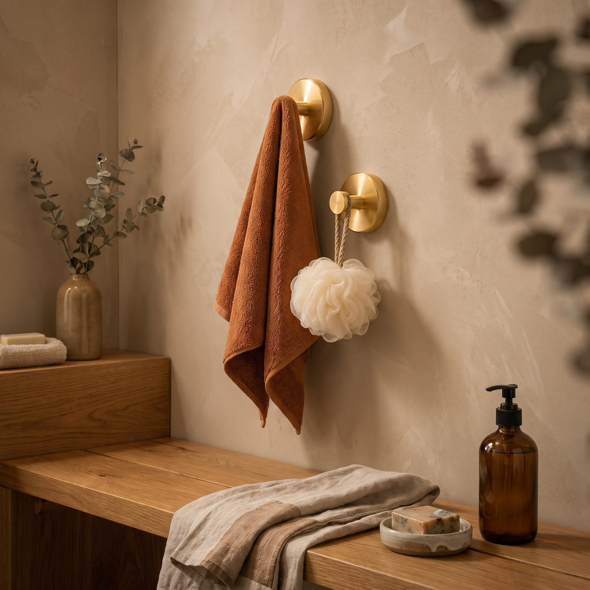 Gold suction wall hooks with a towel and bath sponge in a warm bathroom