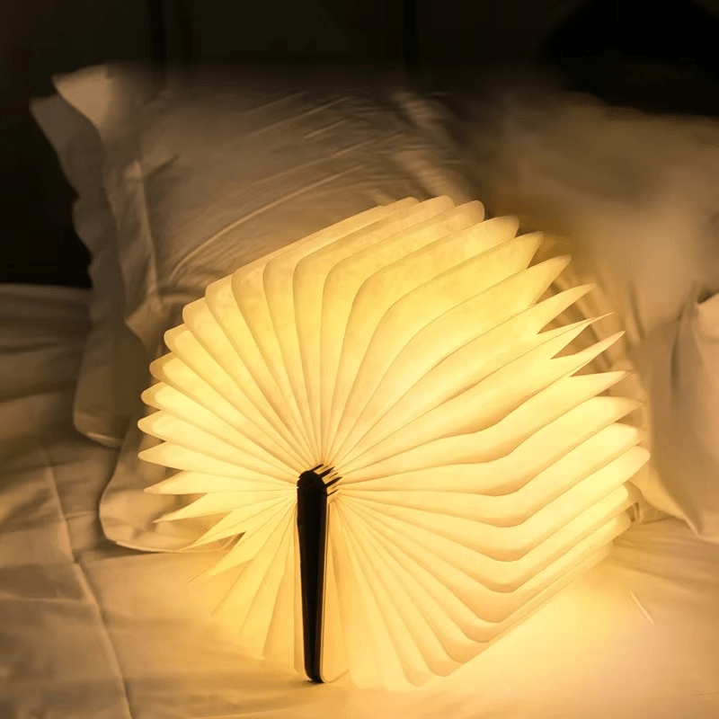 Sula book lamp opened into a glowing fan on a bed in a dark room