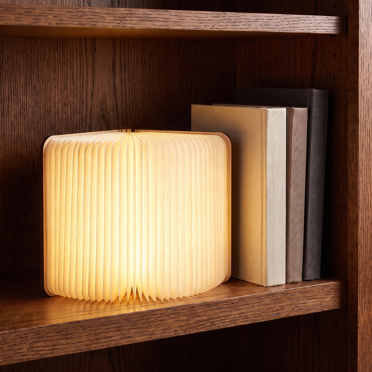 Sula book lamp with light wood covers, standing open and glowing on an oak bookshelf beside books