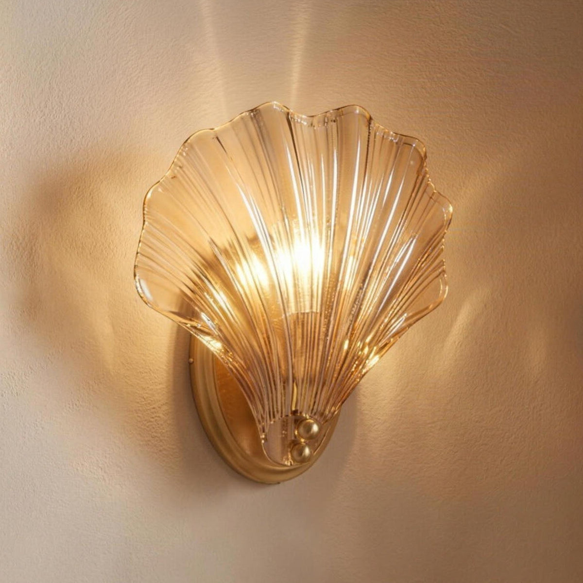 Tyra ribbed glass shell wall sconce glowing on a warm plaster wall