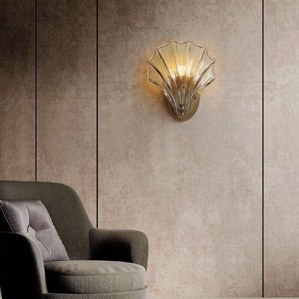 Tyra shell wall sconce lit on a living room wall above an armchair