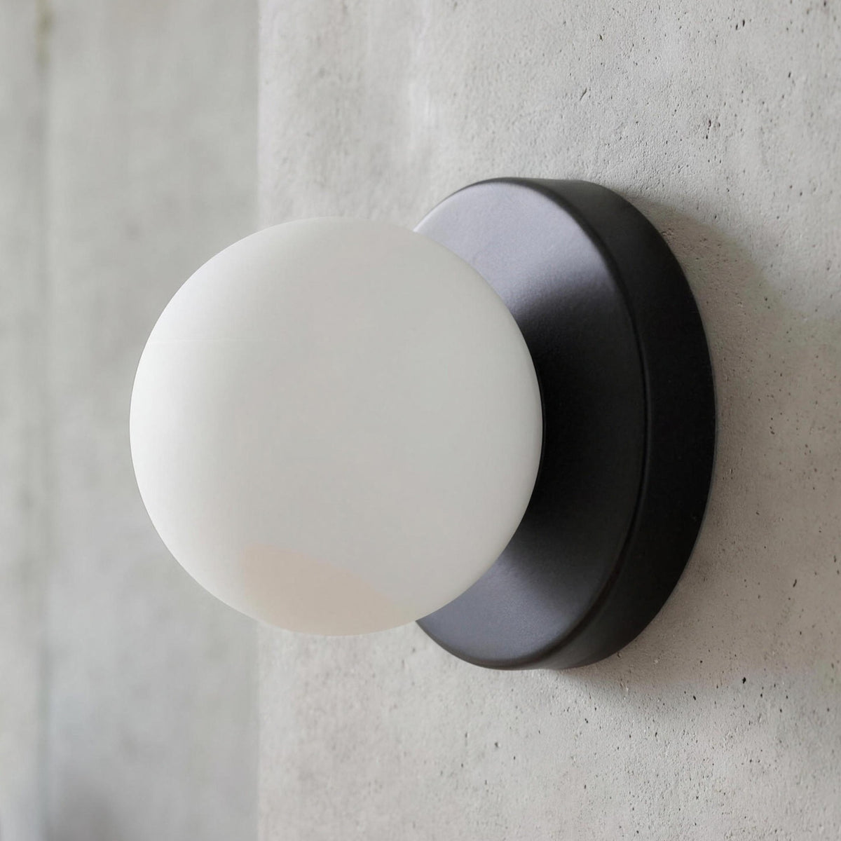 Ulla wall sconce in Black, white glass globe on a round plate against a concrete wall