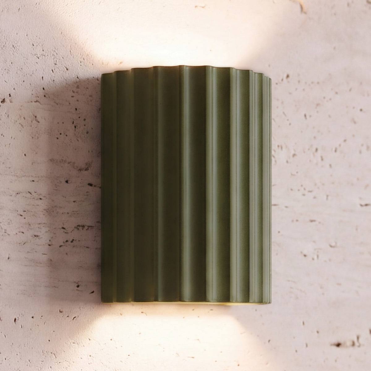 Unni LED wall sconce, green fluted shell, lit up and down on a travertine wall