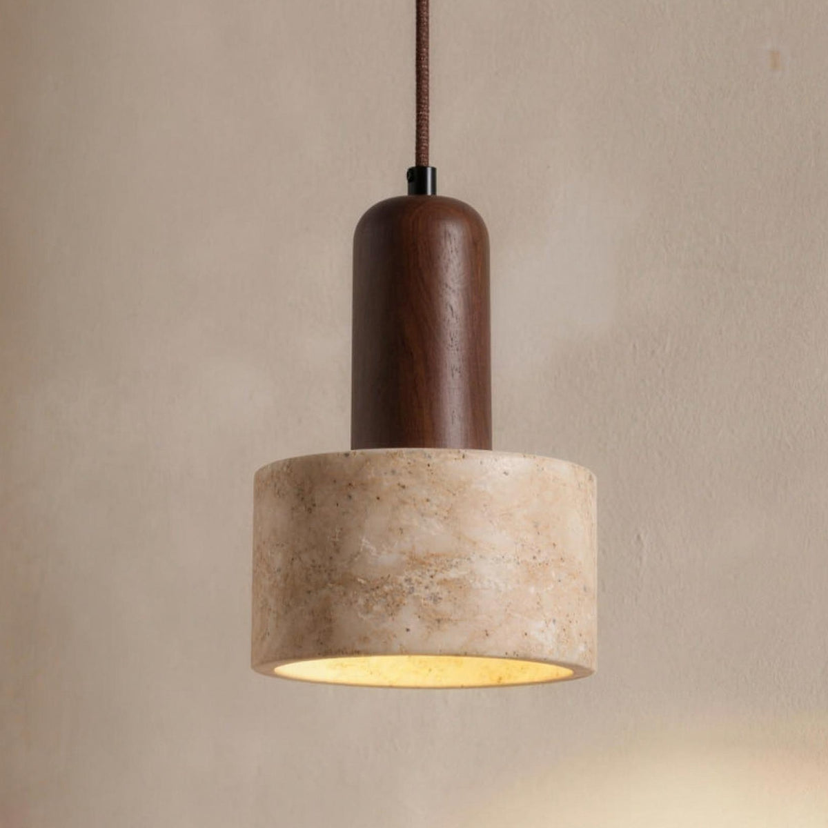 Vanja travertine and walnut pendant light lit over a console