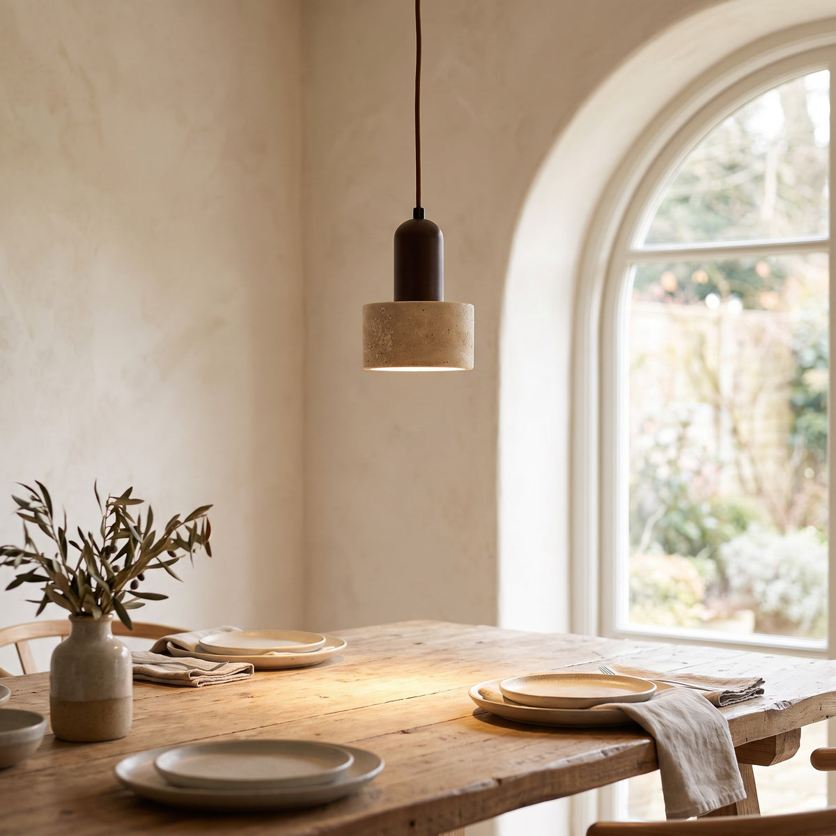 Vanja travertine pendant light lit over a dining table by an arched window