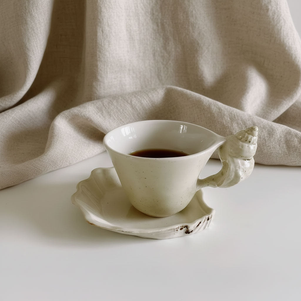 Cup and saucer with black coffee on a white table against a linen backdrop