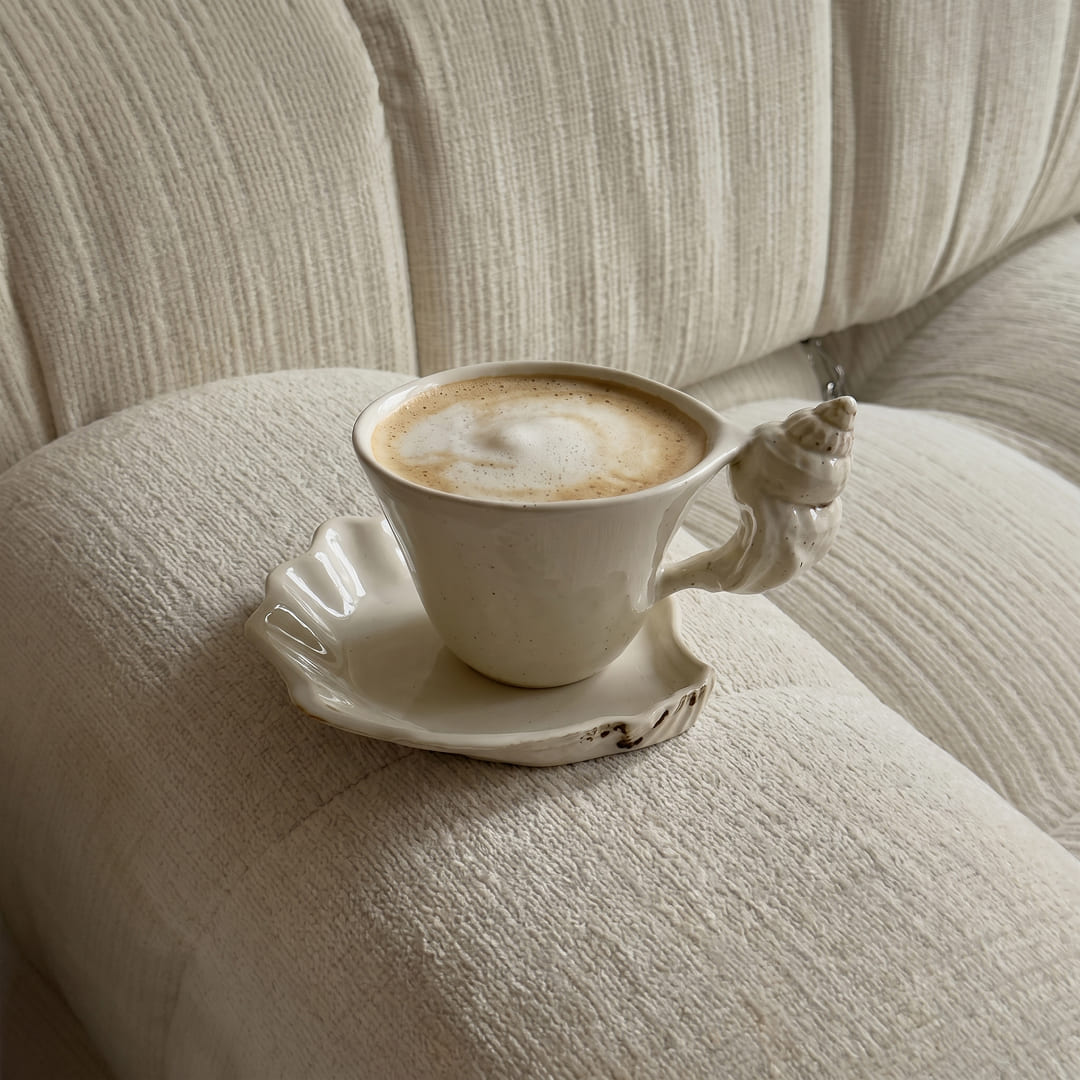 Cappuccino in the shell handle cup resting on a textured cream sofa arm