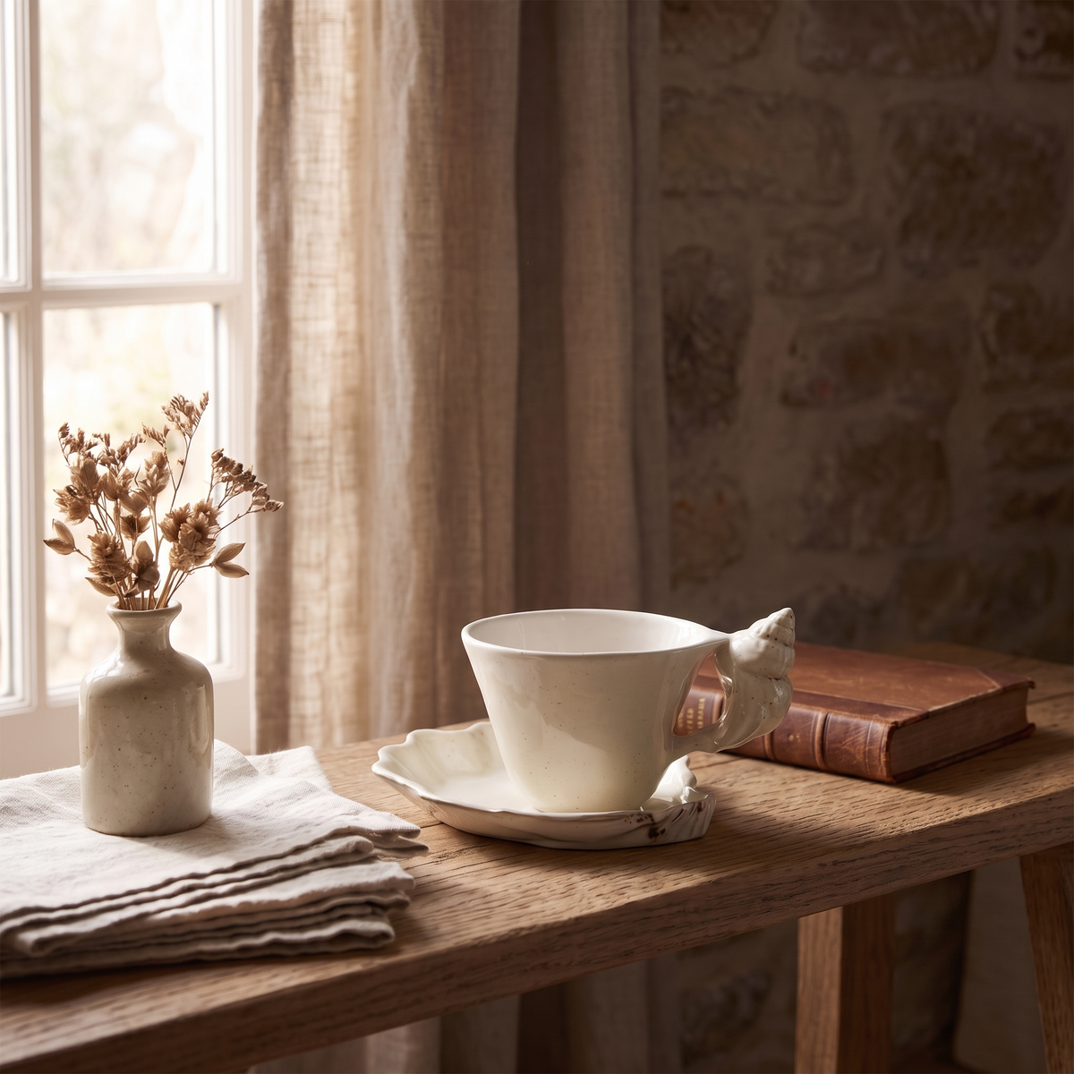 Speckled cream cup and saucer on a wooden bench by a window with dried flowers