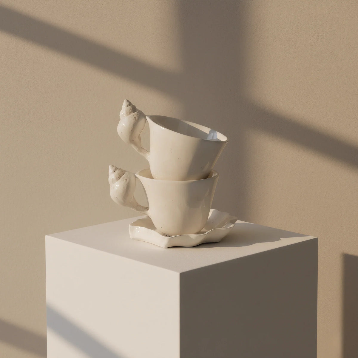 Two cups stacked on one shell saucer on a white plinth in window light