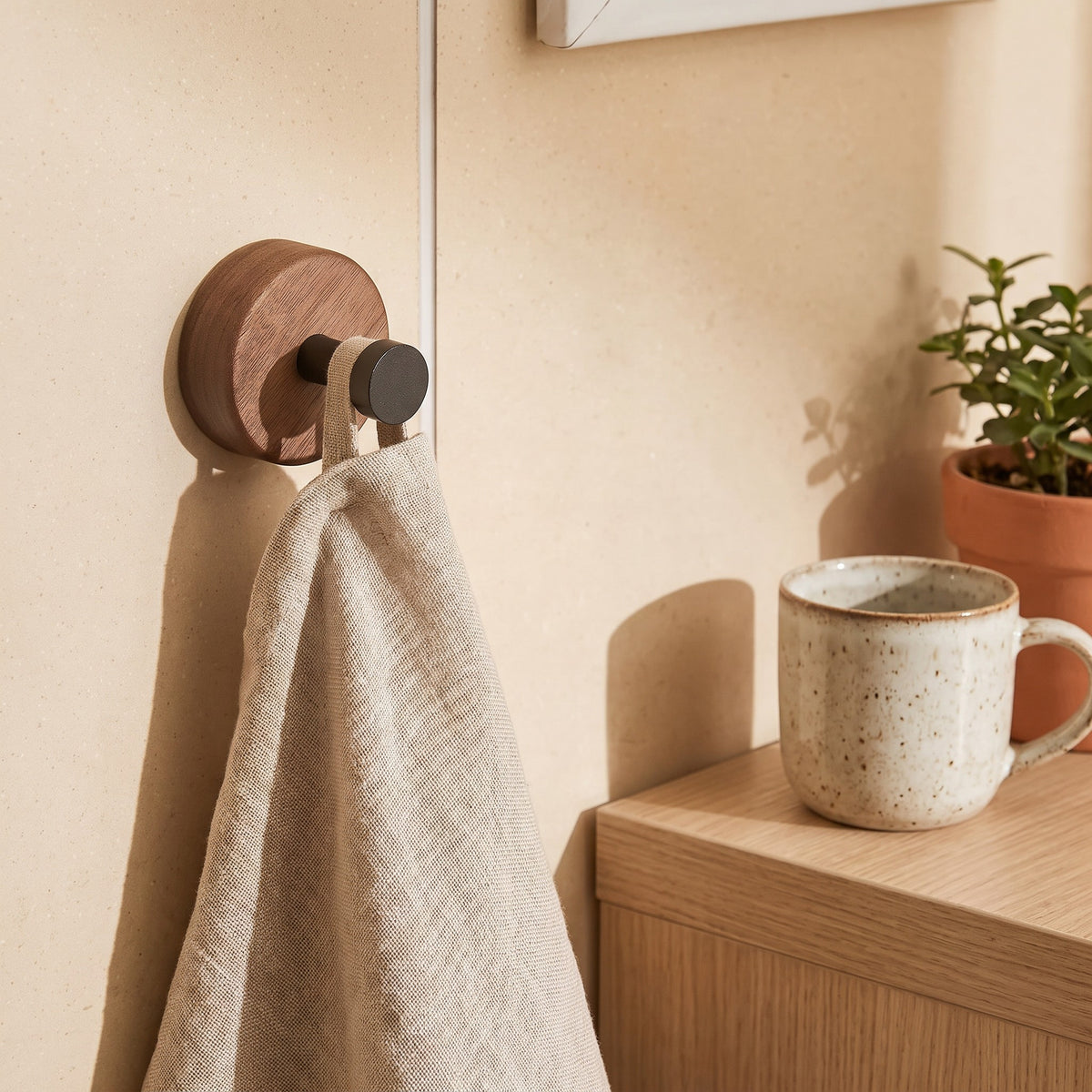 Walnut wall hook holding a linen hand towel in a pale tiled bathroom